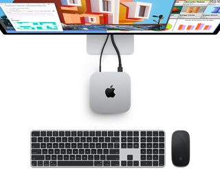Top of silver Mac mini with Apple logo, shown plugged into a monitor and next to a wireless Magic Keyboard and Magic Mouse