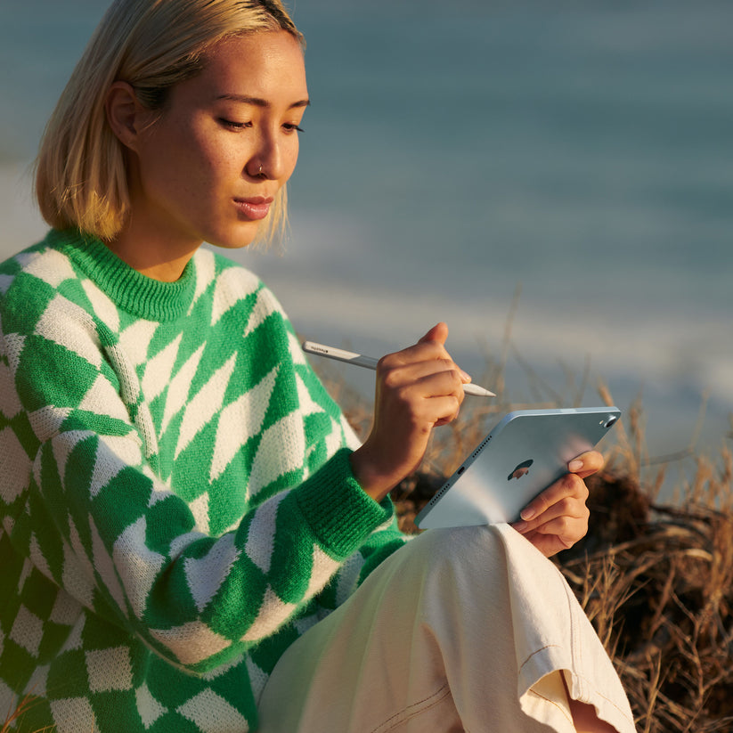 Person using Apple Pencil Pro with iPad mini outdoors by the beach